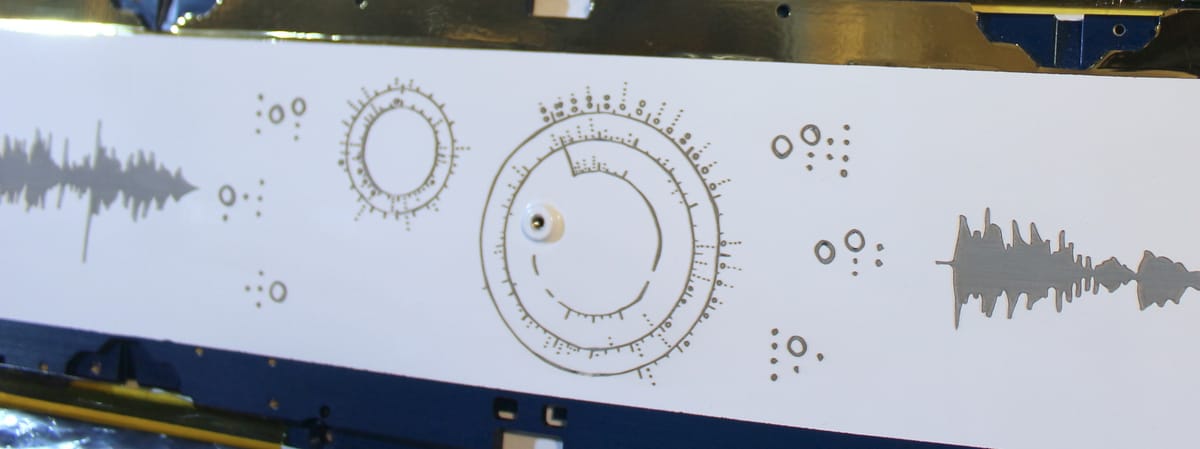 A rectangular aluminum satellite panel, with my circular "iris" notation etched into its white coating, along with chords and audio waveforms.